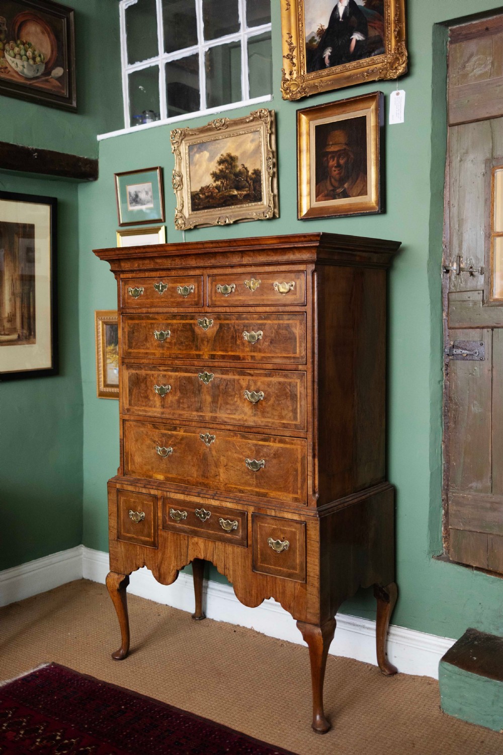 An early 18th-century walnut chest on stand with multiple crossbanded drawers, brass handles, a scalloped apron, and cabriole legs. View II