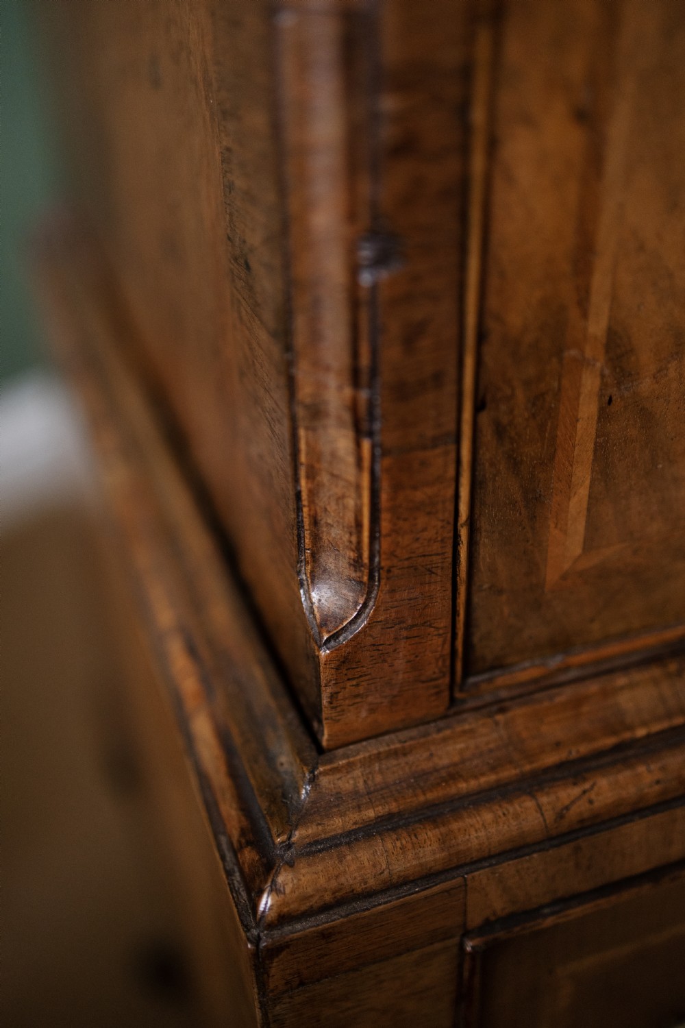 An early 18th-century walnut chest on stand with multiple crossbanded drawers, brass handles, a scalloped apron, and cabriole legs. View IV