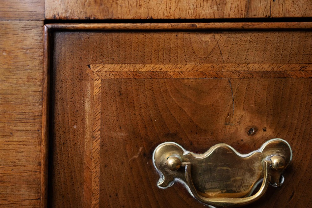 An early 18th-century walnut chest on stand with multiple crossbanded drawers, brass handles, a scalloped apron, and cabriole legs. View V