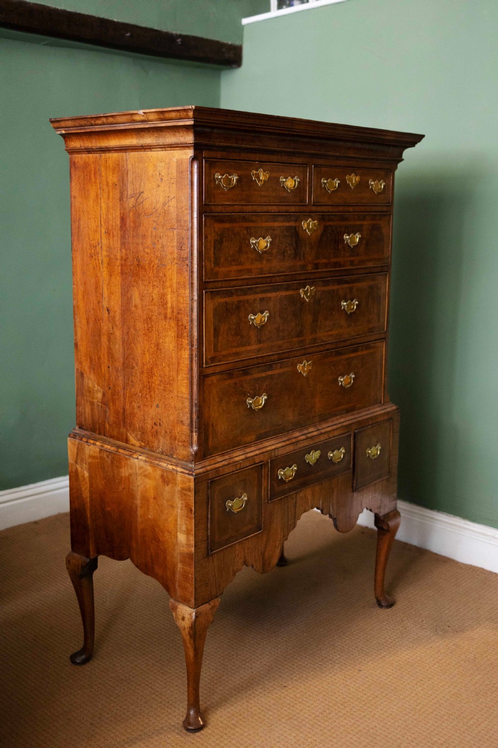 An early 18th-century walnut chest on stand with multiple crossbanded drawers, brass handles, a scalloped apron, and cabriole legs. View VI