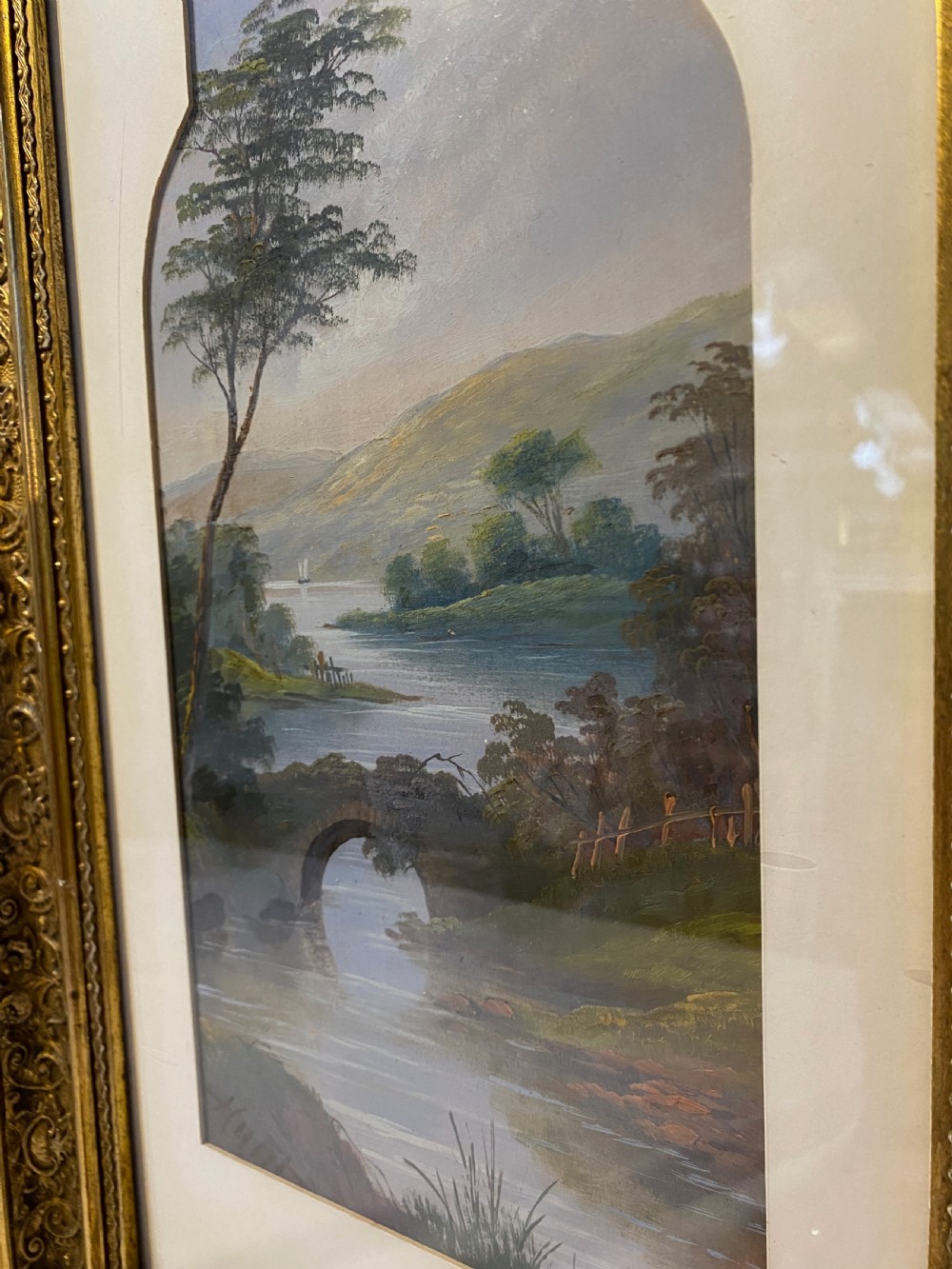 An antique watercolour painting depicting a river landscape with an arched bridge, set within a pointed arch aperture mount and a richly decorated gilt rectangular frame. View II