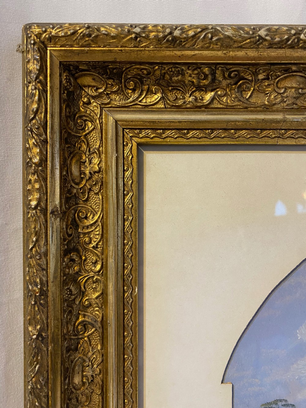 An antique watercolour painting depicting a river landscape with an arched bridge, set within a pointed arch aperture mount and a richly decorated gilt rectangular frame. View IV