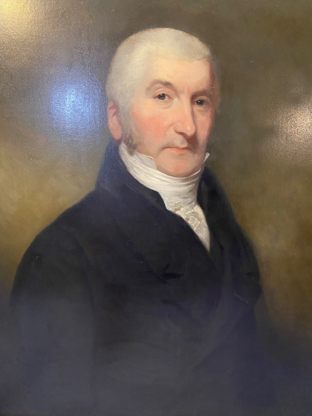 An 18th-century oil portrait painting depicting a gentleman wearing a dark coat and white cravat set in a gilt moulding frame. View III