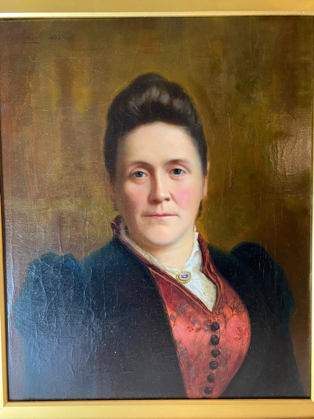 A nineteenth-century oil painting depicting a woman in a dark jacket and red bodice, framed within an ornamental gilt wood frame. View II
