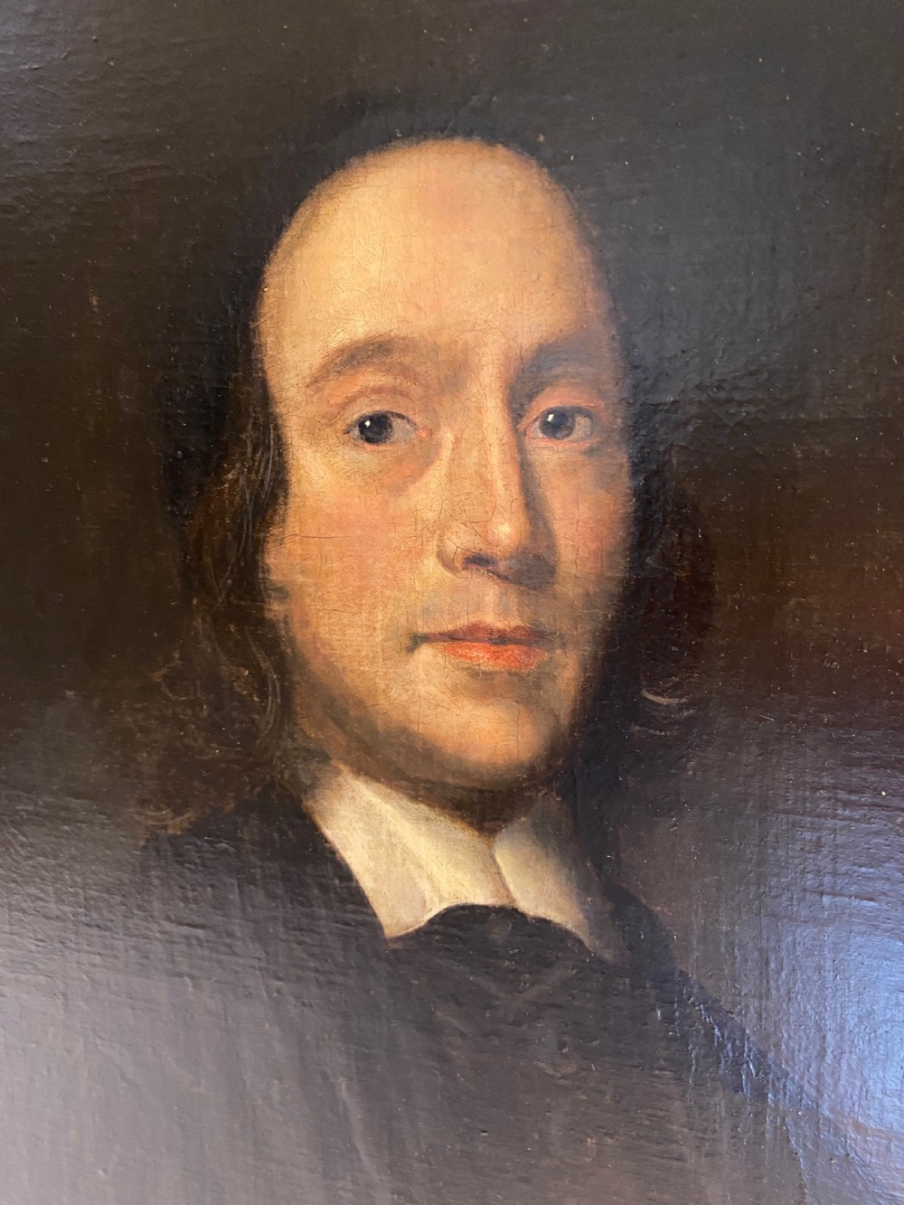 An oil portrait of a 17th-century clergyman wearing a black robe and white collar, set inside an ornate carved gold frame. View II