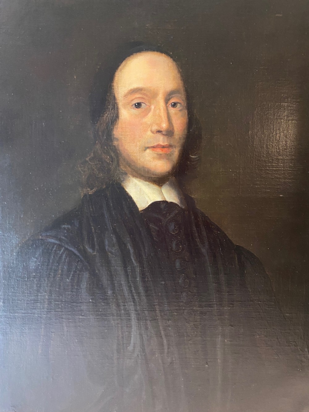 An oil portrait of a 17th-century clergyman wearing a black robe and white collar, set inside an ornate carved gold frame. View III