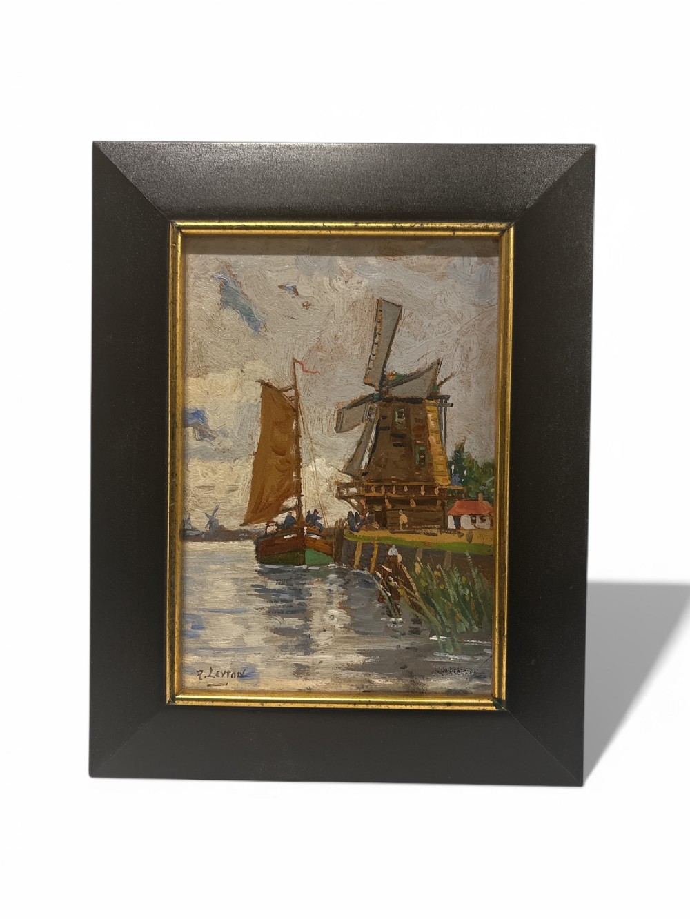 An early twentieth-century framed impressionist oil painting depicting a brown sailboat beside a wooden windmill along a waterway under a cloudy sky.