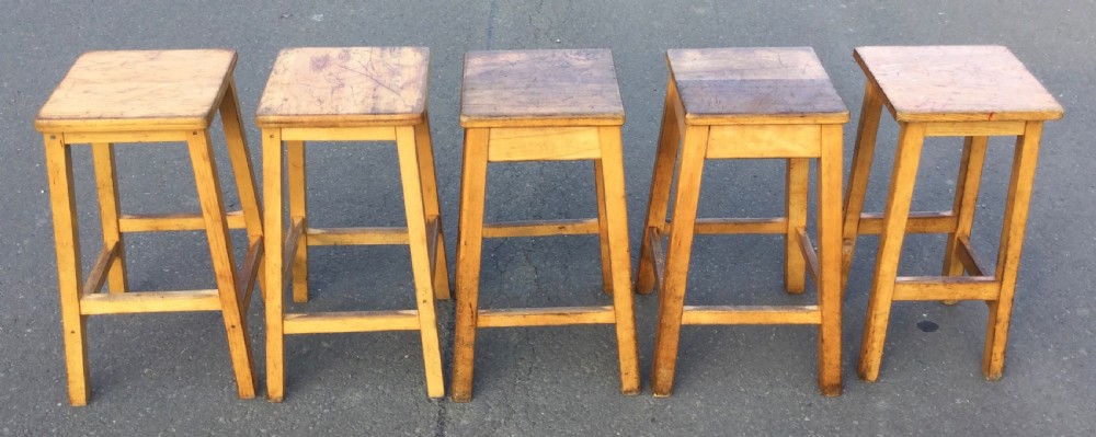 A row of five vintage wooden high stools featuring square flat seats, splayed legs, and four-sided footrest stretchers. View III