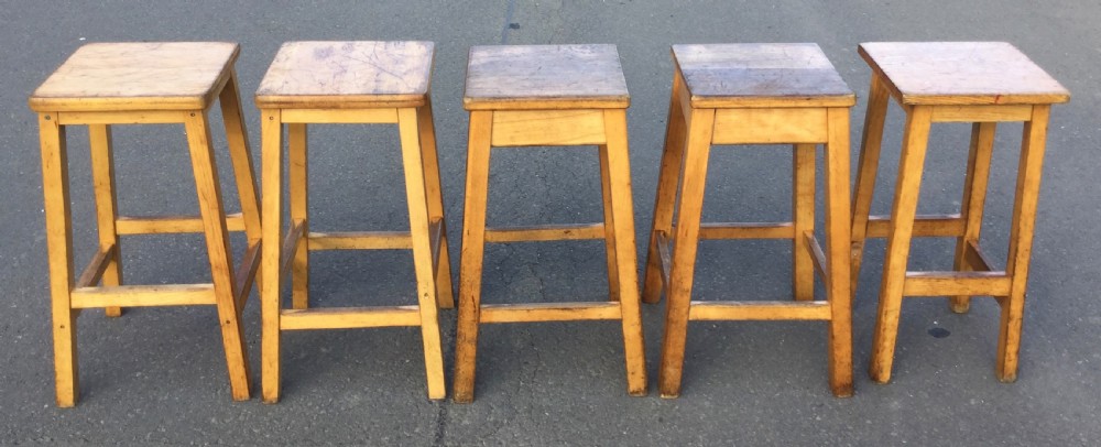 A row of five vintage wooden high stools featuring square flat seats, splayed legs, and four-sided footrest stretchers. View IV