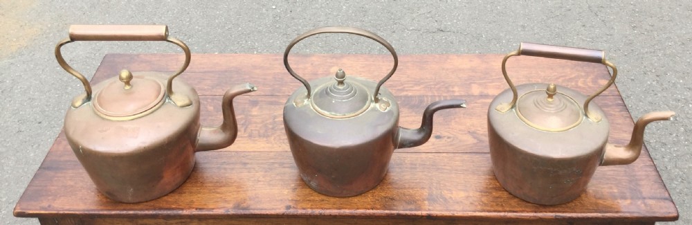 A set of three 19th-century Victorian copper tea kettles with brass handles displayed side by side.