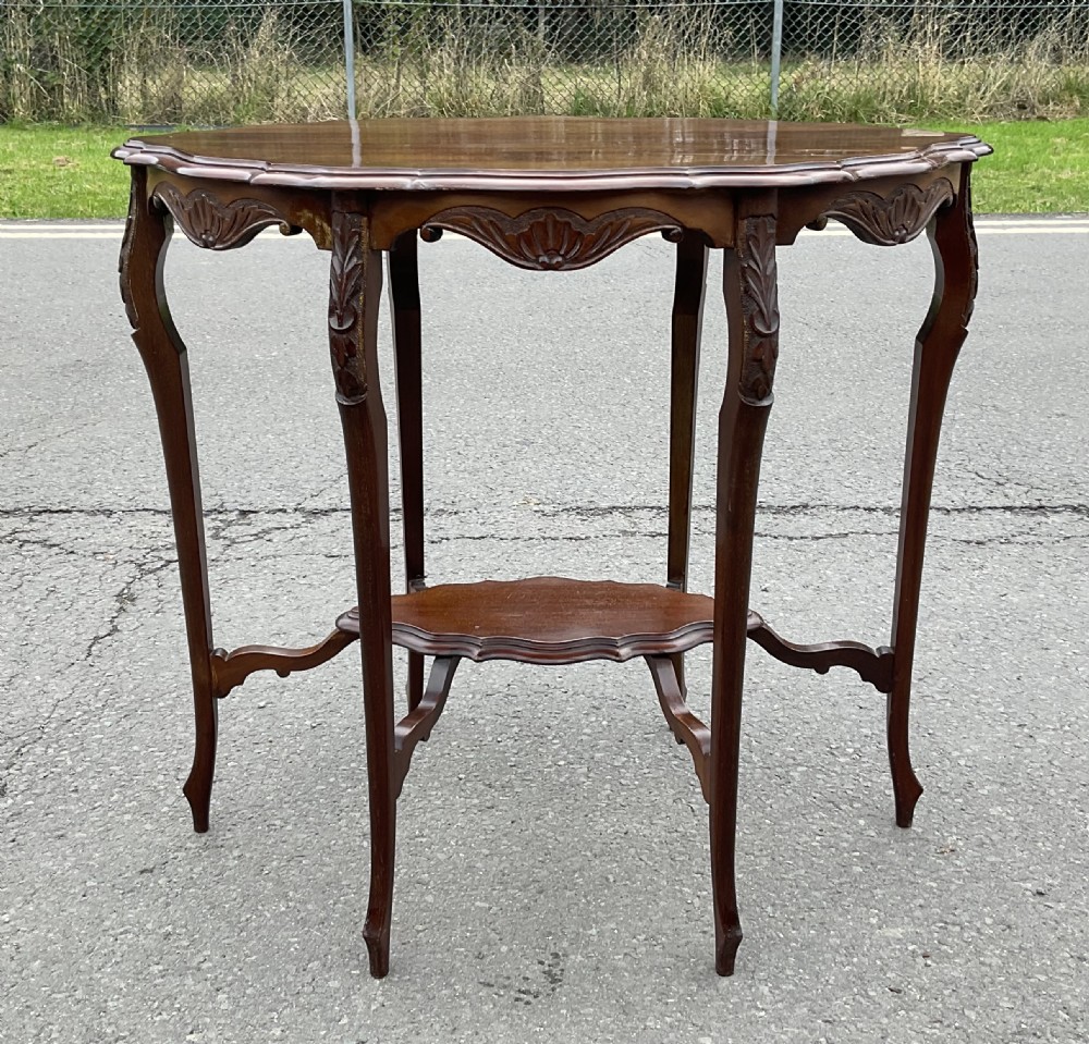 An Edwardian mahogany oval occasional table featuring a scalloped rim, carved frieze apron, slender cabriole legs, and a lower undertier shelf. View VII