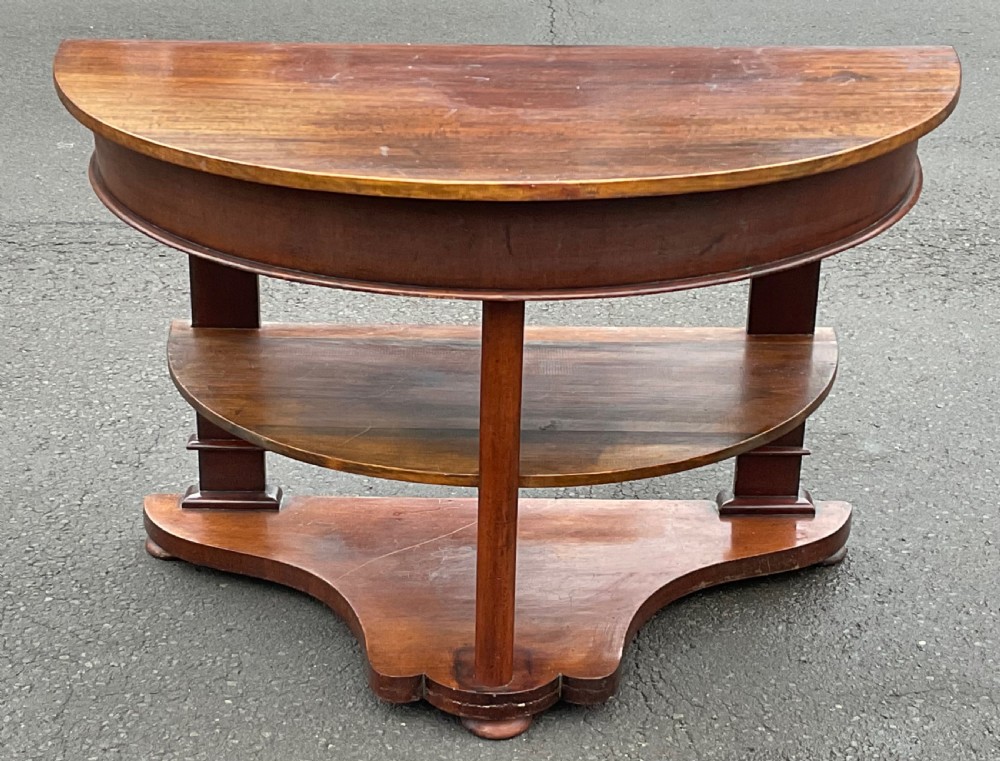A Victorian mahogany demi-lune console table featuring a semicircular top, an intermediate tier shelf, and a shaped plinth base.