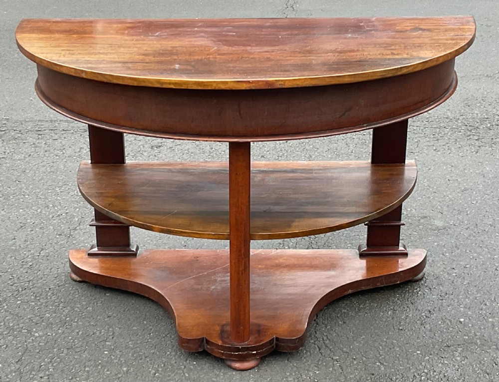 A Victorian mahogany demi-lune console table featuring a semicircular top, an intermediate tier shelf, and a shaped plinth base. View IV