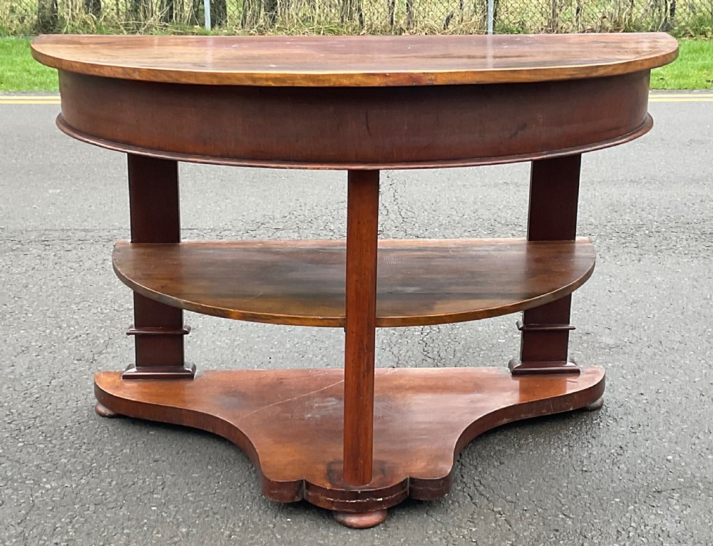 A Victorian mahogany demi-lune console table featuring a semicircular top, an intermediate tier shelf, and a shaped plinth base. View V