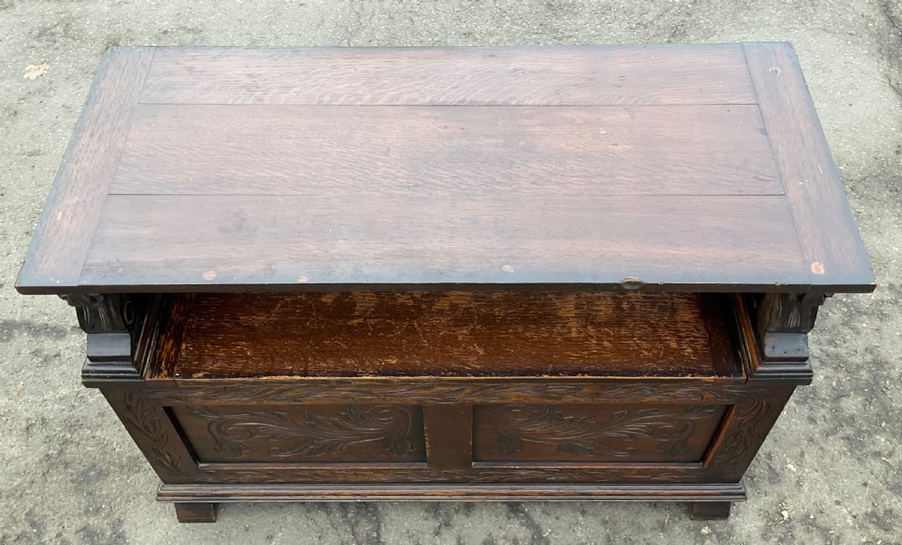 A dark oak monks bench featuring foliate scroll carving on the backrest and base panels, carved lion head armrests, and a hinged lift-up seat. View VIII
