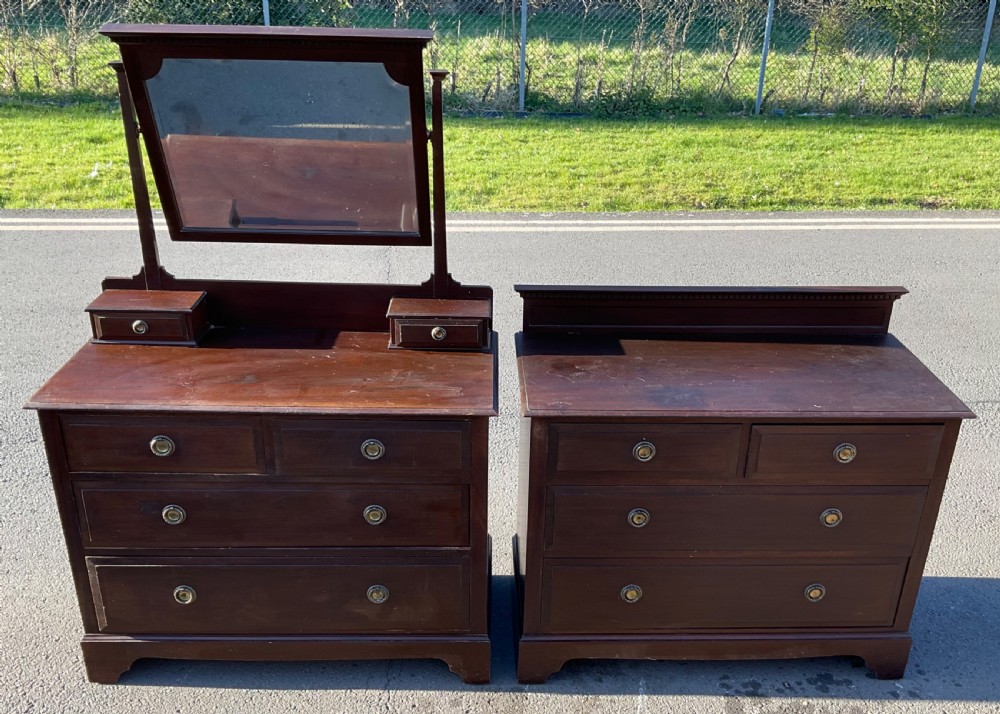 A pair of dark Edwardian mahogany furniture pieces featuring a dressing chest with a tilting mirror alongside a matching chest of drawers.