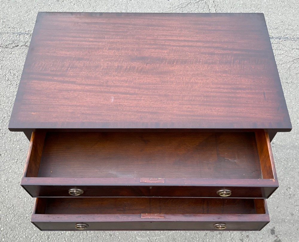 An Edwardian mahogany two-drawer chest featuring brass ring drop handles, flame mahogany veneer, and long tapered legs. View IV