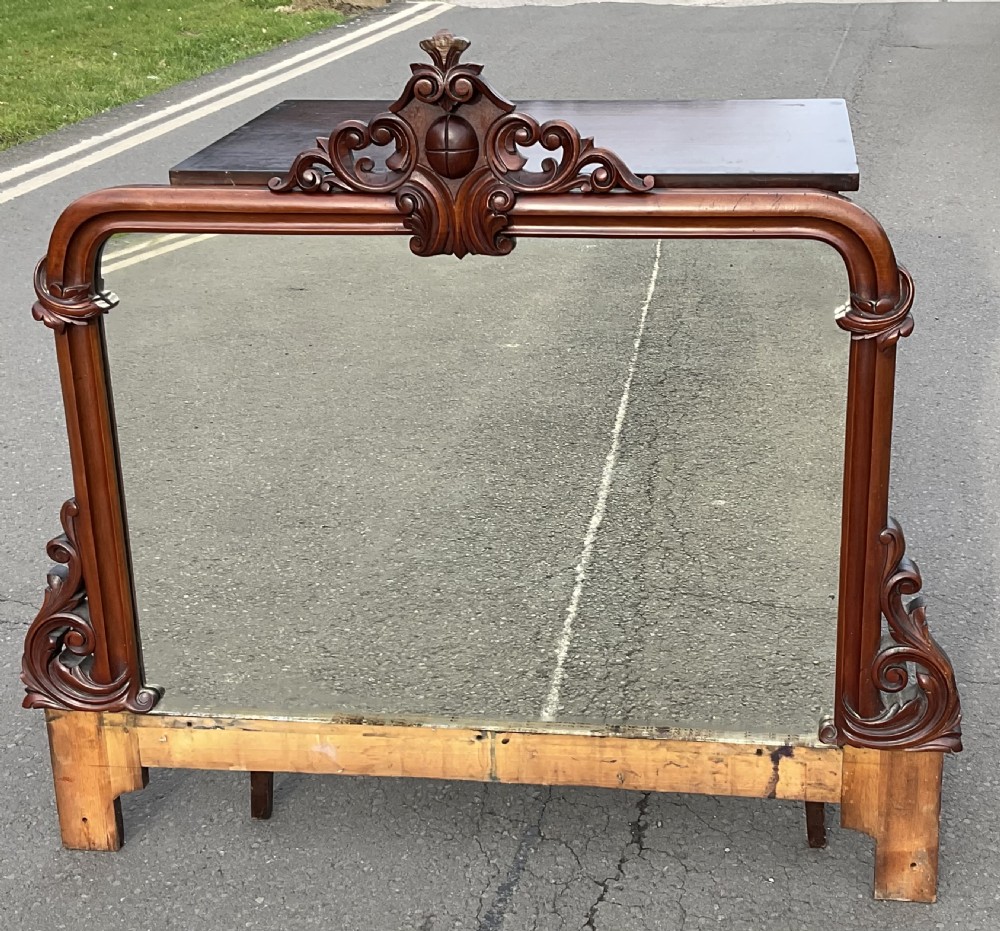 A Victorian mahogany overmantel mirror featuring a carved central crest with scrollwork detail and side brackets.