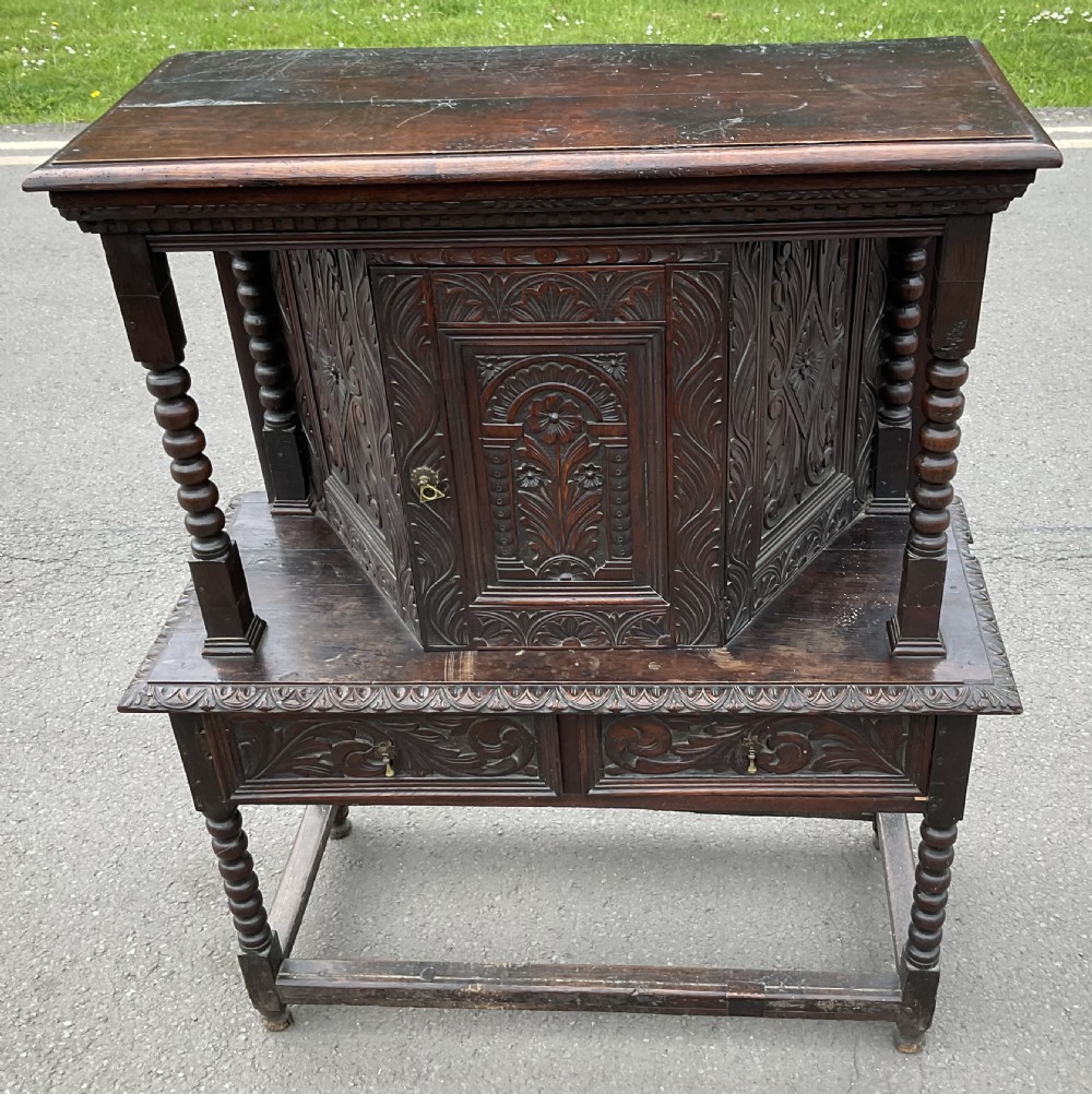 A dark Victorian carved oak court cupboard featuring a canted upper cabinet over two carved drawers and bobbin turned supports. View V