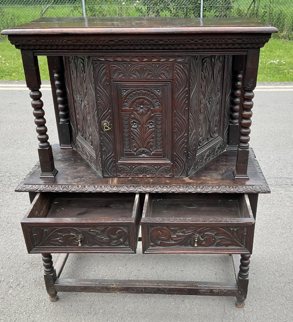 A dark Victorian carved oak court cupboard featuring a canted upper cabinet over two carved drawers and bobbin turned supports. View VI