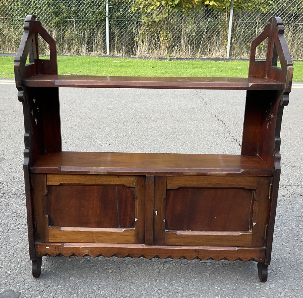 A dark mahogany wall-mounted shelf unit featuring a two-door lower cupboard, open upper shelves, gothic arch side supports, and a scalloped lower trim.