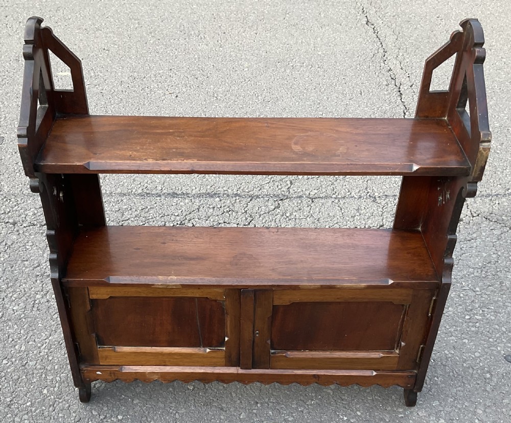 A dark mahogany wall-mounted shelf unit featuring a two-door lower cupboard, open upper shelves, gothic arch side supports, and a scalloped lower trim. View II
