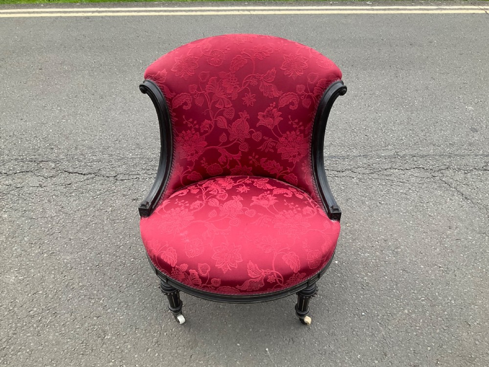Victorian Aesthetic Movement nursing chair featuring a black ebonised wood frame, turned legs on casters, and red damask upholstery. View II