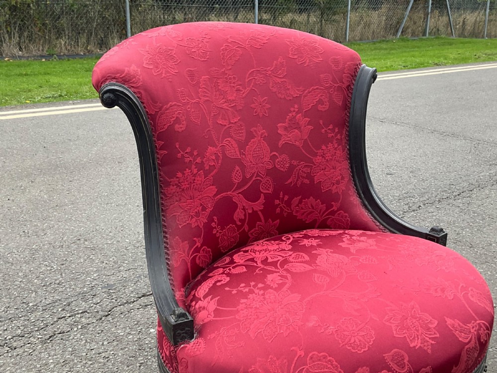 Victorian Aesthetic Movement nursing chair featuring a black ebonised wood frame, turned legs on casters, and red damask upholstery. View III