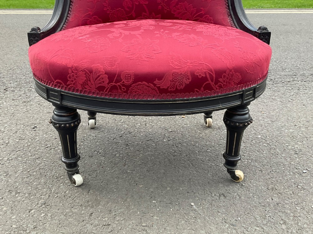 Victorian Aesthetic Movement nursing chair featuring a black ebonised wood frame, turned legs on casters, and red damask upholstery. View IV