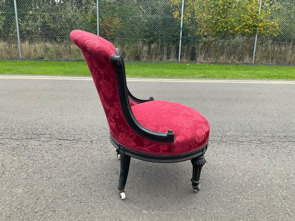 Victorian Aesthetic Movement nursing chair featuring a black ebonised wood frame, turned legs on casters, and red damask upholstery. View IX