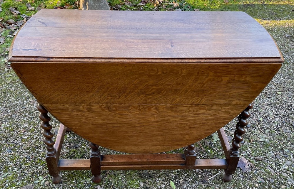 An oak drop-leaf gateleg dining table featuring turned barley twist legs and a dark warm wood finish shown with leaves folded.