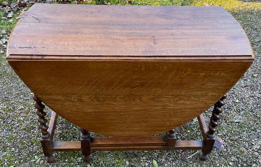 An oak drop-leaf gateleg dining table featuring turned barley twist legs and a dark warm wood finish shown with leaves folded. View III