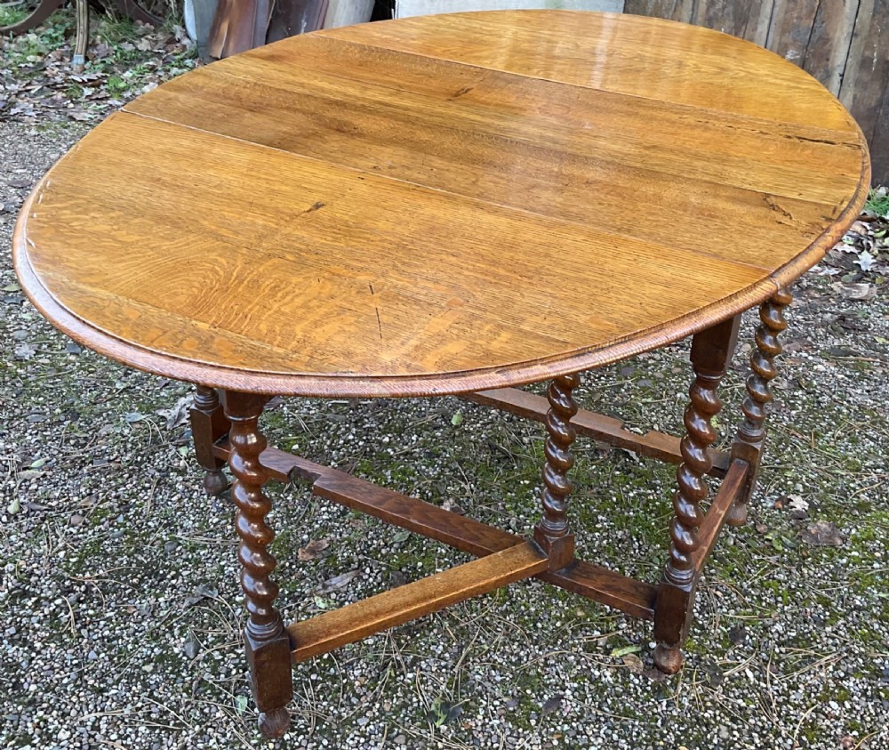 An oak drop-leaf gateleg dining table featuring turned barley twist legs and a dark warm wood finish shown with leaves folded. View IV
