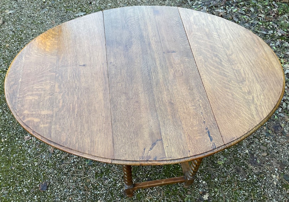 An oak drop-leaf gateleg dining table featuring turned barley twist legs and a dark warm wood finish shown with leaves folded. View V