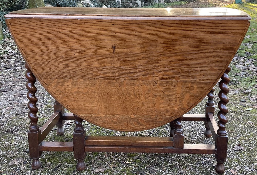 An oak drop-leaf gateleg dining table featuring turned barley twist legs and a dark warm wood finish shown with leaves folded. View VII