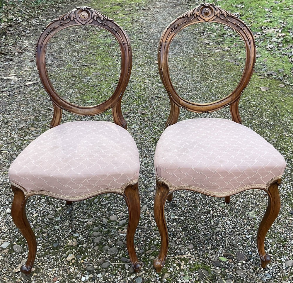 A pair of Victorian carved walnut balloon back dining chairs featuring padded pink fabric seats and cabriole legs.