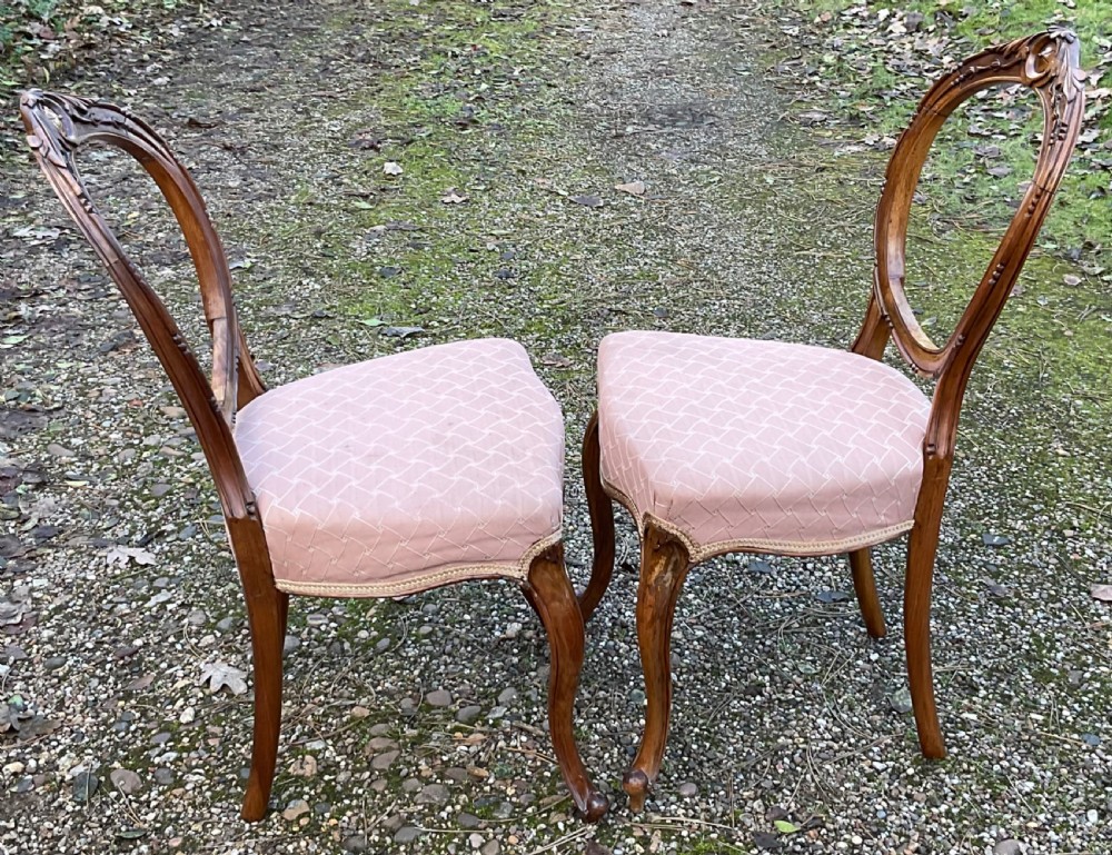A pair of Victorian carved walnut balloon back dining chairs featuring padded pink fabric seats and cabriole legs. View VII