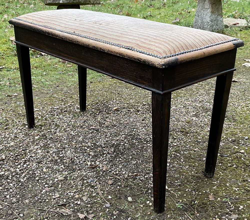 An Edwardian dark mahogany duet piano stool featuring four tapered legs and a padded striped fabric seat trimmed with brass studs. View IV