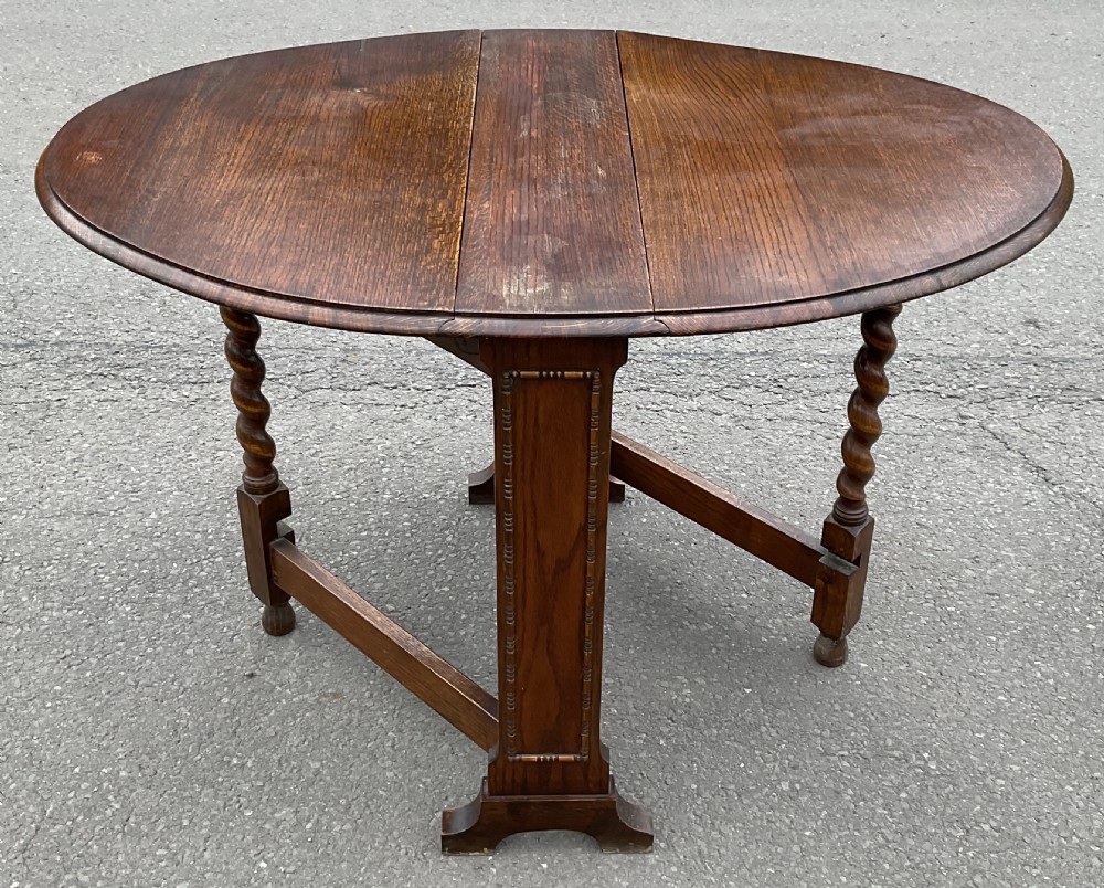 A solid oak drop-leaf dining table shown in a folded compact position. View VII