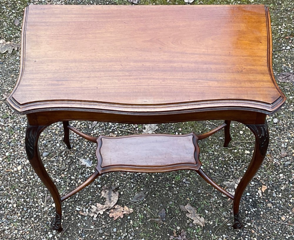 An Edwardian mahogany foldover card table featuring a shaped serpentine top, carved cabriole legs, and a lower tier shelf. View IV