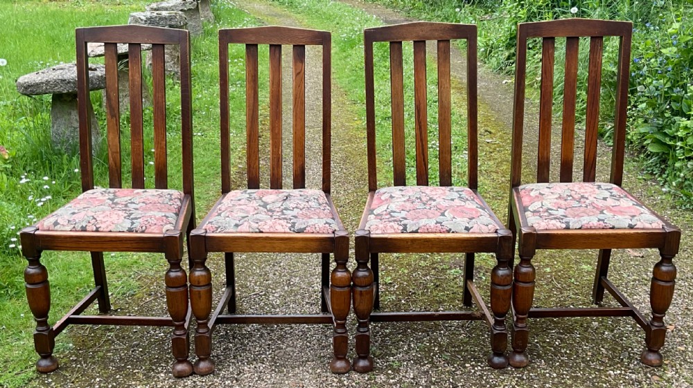 A set of four dark oak dining chairs featuring high slatted backs, turned front legs, and floral upholstered drop-in seats.