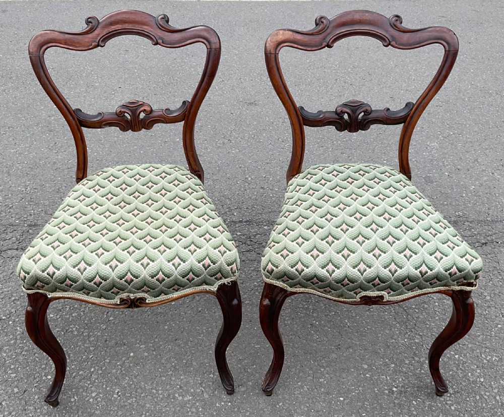 A pair of Victorian rosewood dining chairs featuring carved balloon backs, green patterned upholstered seats, and cabriole front legs.