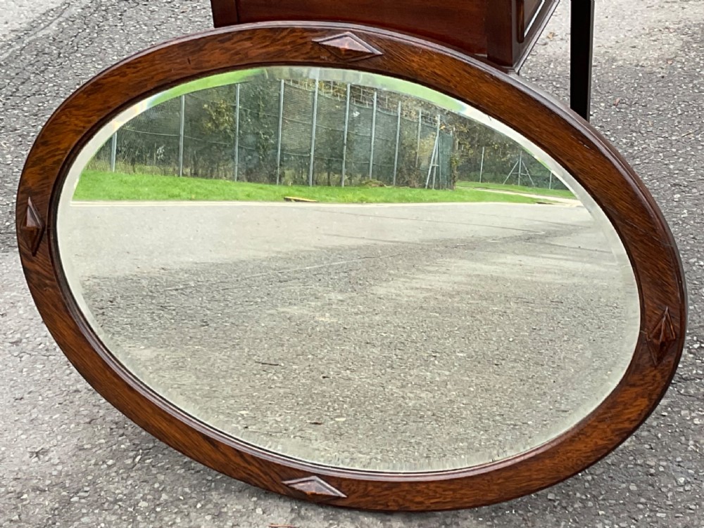 An oval wall mirror set in a warm brown oak frame featuring four carved diamond motifs and a bevelled glass edge.