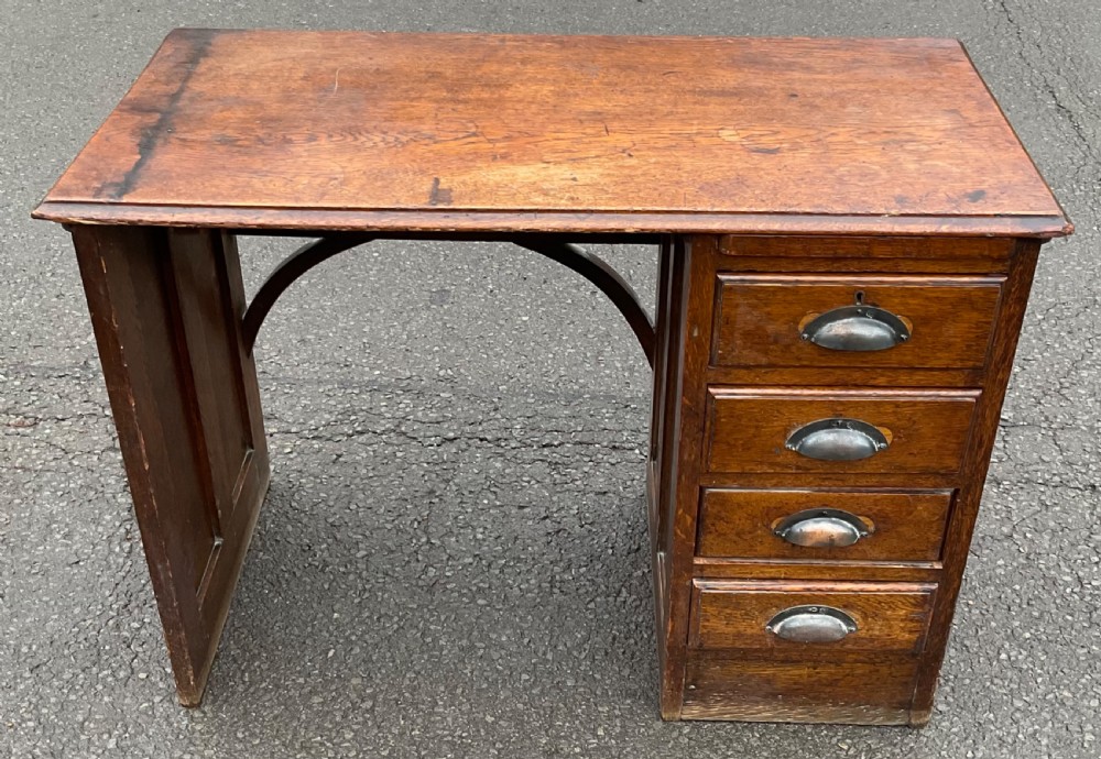 An Edwardian oak writing desk featuring a flat rectangular top, four right-hand drawers with metal cup handles, and an open left kneehole section with arched supports.