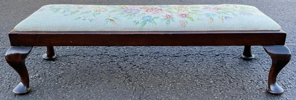 A long rectangular mahogany footstool with light green floral needlepoint upholstery, supported by four cabriole legs with pad feet.