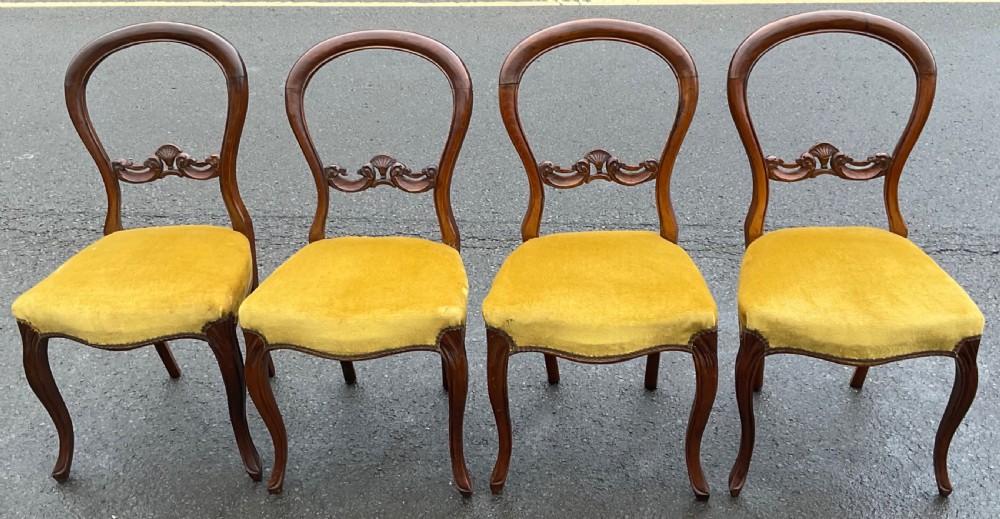 A set of four Victorian walnut balloon-back side chairs with carved central splats and mustard yellow velvet upholstered seats.