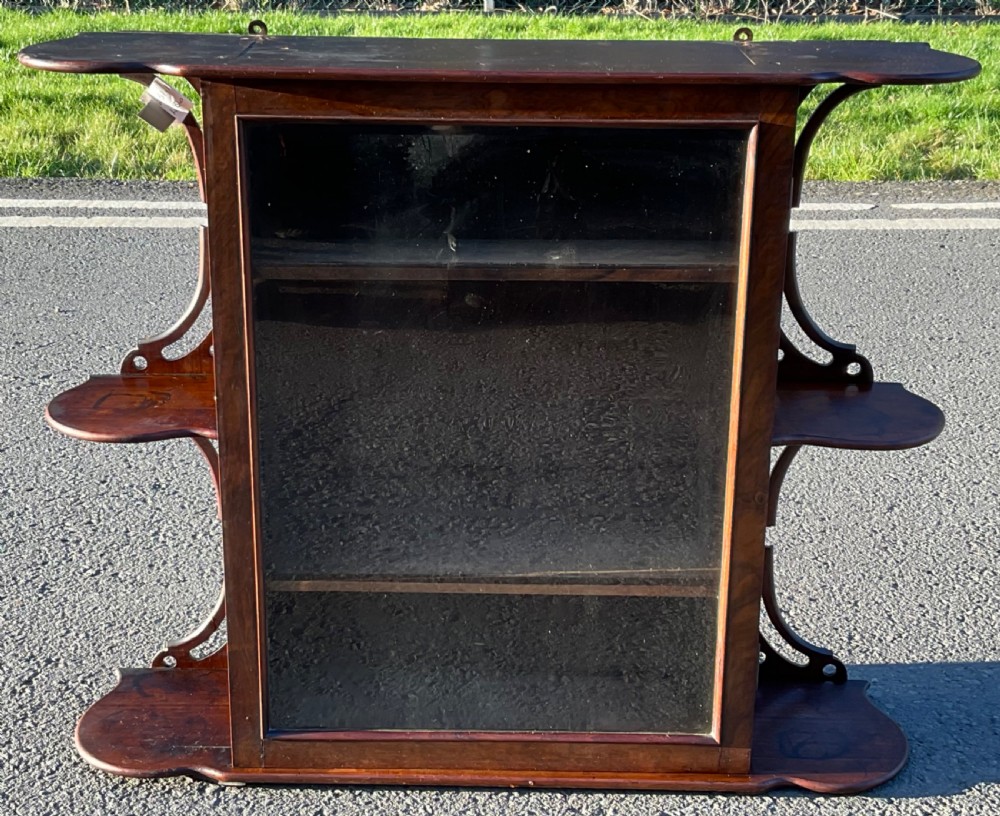 A Victorian dark mahogany hanging wall cabinet featuring a central glass door flanked by tiered open side shelves.