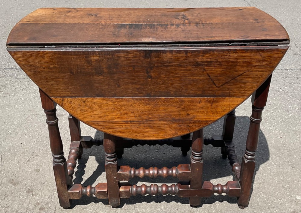 A small antique oak gateleg table featuring hinged drop-leaf flaps, hand-turned legs, and lower stretchers with a warm brown finish.