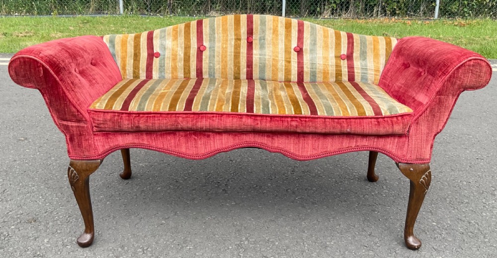 An upholstered window seat featuring red and striped velvet fabric with scroll arms, button tufting, and carved walnut cabriole legs.