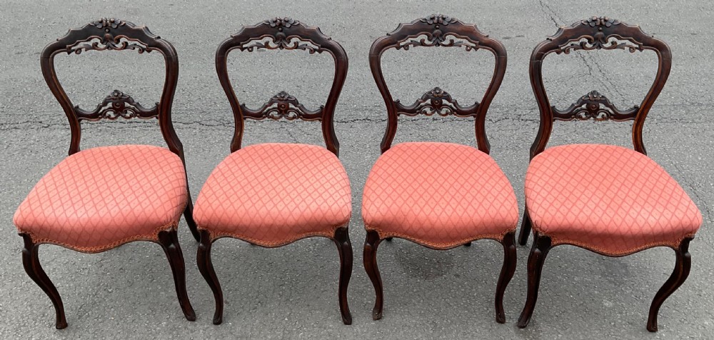 A set of four Victorian walnut balloon-back dining chairs featuring carved cross-bars, front cabriole legs, and coral patterned upholstery.